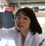 Headshot of Dr. Xu Zhang in a white lab coat reaching for a tool